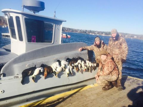 Three hunters display their sea ducks on the side of the boat