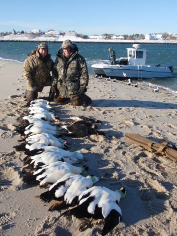 Hunters display eiders with hunting boat in background